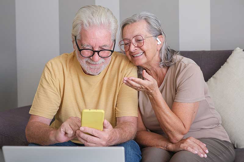 Older adults sitting together and using a smartphone at home, representing everyday life and connection similar to Westhaven Community in Boone, Iowa.