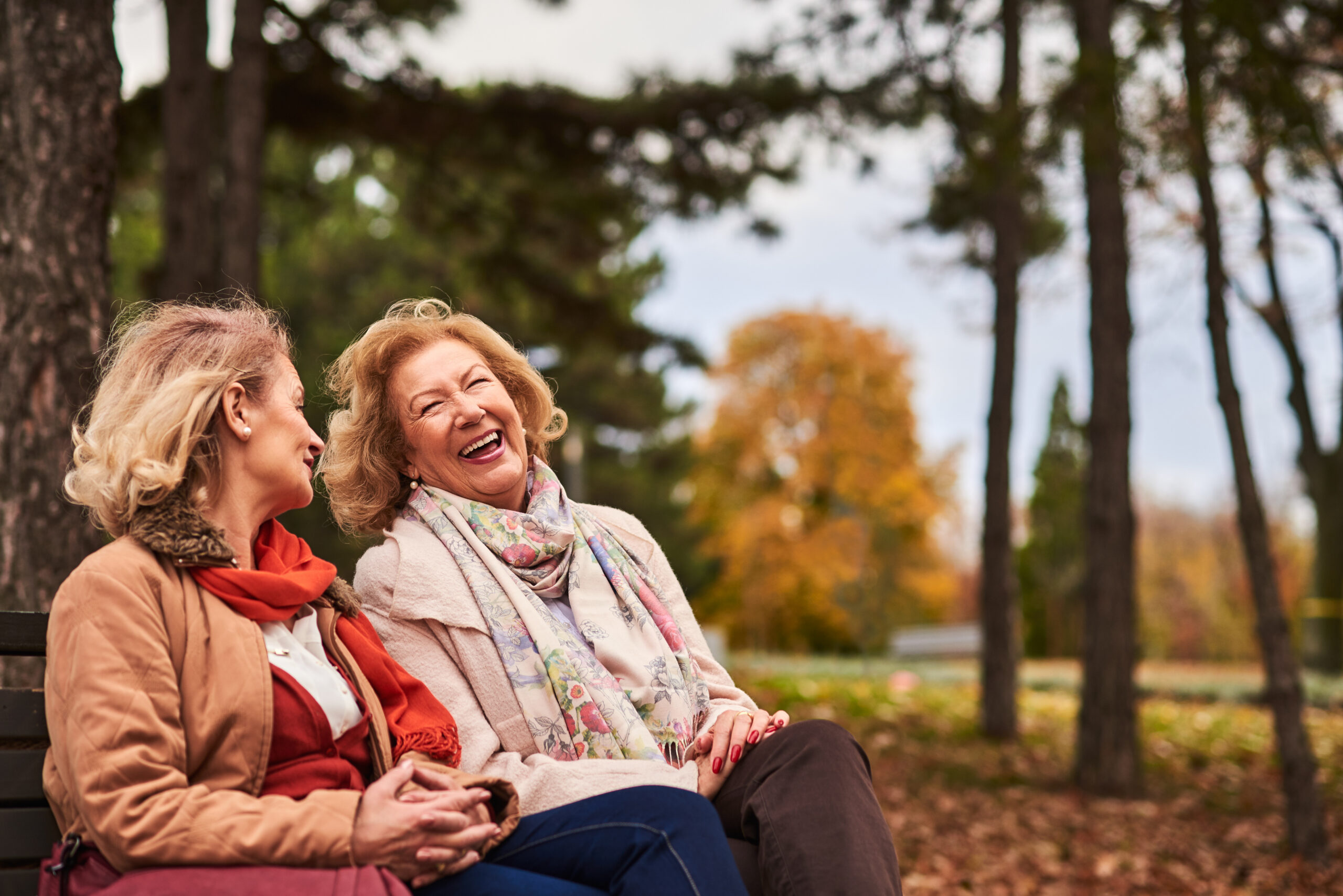 Two older adults sitting outdoors in a park with fall colors, talking and smiling at Westhaven Senior Living in Boone, Iowa, highlighting a welcoming senior living community.