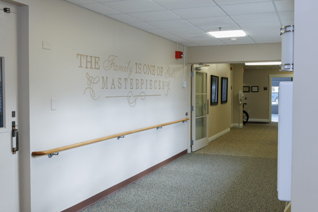Hallway at Westhaven Community in Boone, Iowa with handrail, wall decal quote, and access to resident rooms and common areas.
